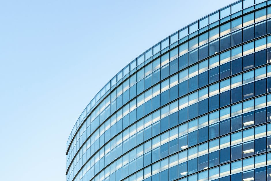 Low angle view of a modern glass office building against a clear blue sky.