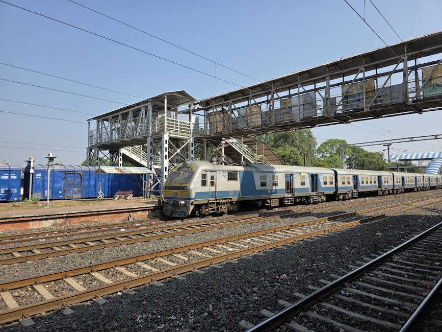 Pune Theatre Show Revives History and Magic of Deccan Queen Train Passenger train moving under a pedestrian bridge at an outdoor railway station.