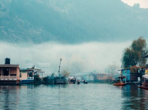 Peaceful boathouses on misty Dal Lake in Jammu, surrounded by fog and mountains.