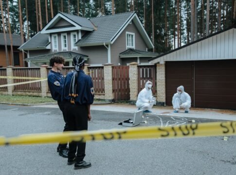 Police and forensic experts examining a crime scene in front of suburban houses.