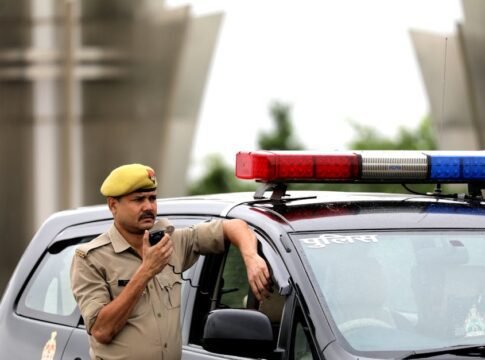 Police officer standing beside patrol car holding a radio microphone outdoors.