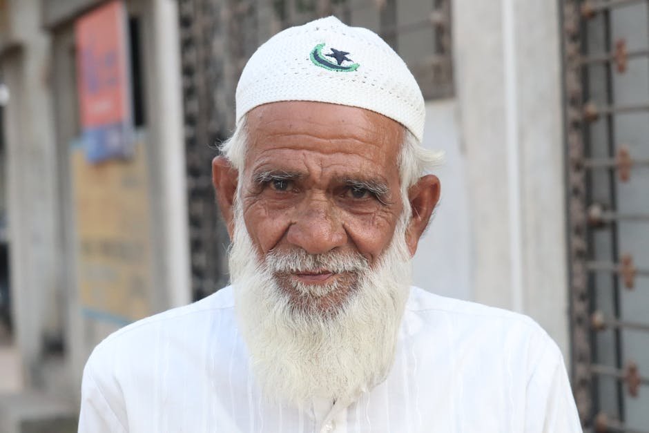 Srinagar Welcomes Tonga Revival After Decades, Preserving Heritage Portrait of an elderly man wearing traditional Muslim attire, featuring a white cap and beard.