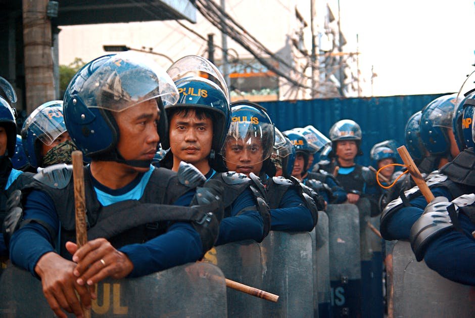 Riot police officers lined up with helmets and shields, maintaining order in a city setting.