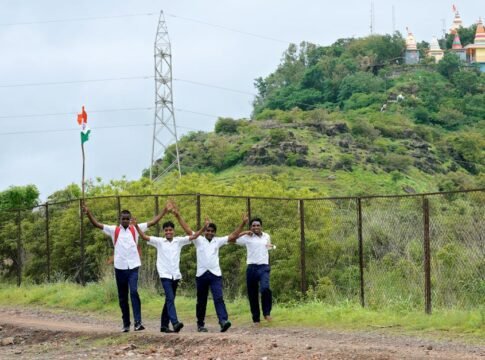 School boys in uniform walking joyfully outdoors with an Indian flag, near a lush hill in Pune, India.