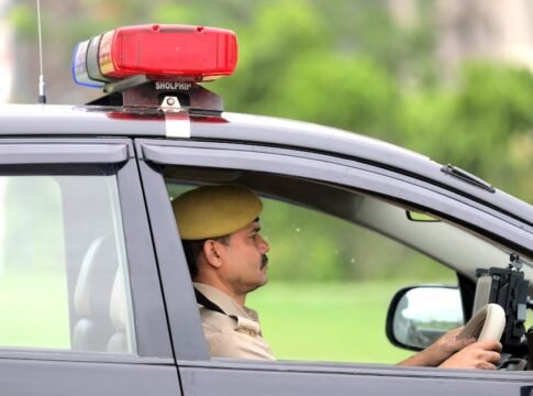 Side view of a police officer driving a patrol car with a visible siren outdoors.
