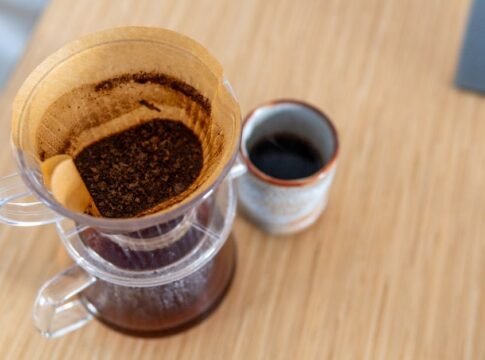 Top-down view of pour-over coffee in a filter next to a ceramic mug on a wooden table.