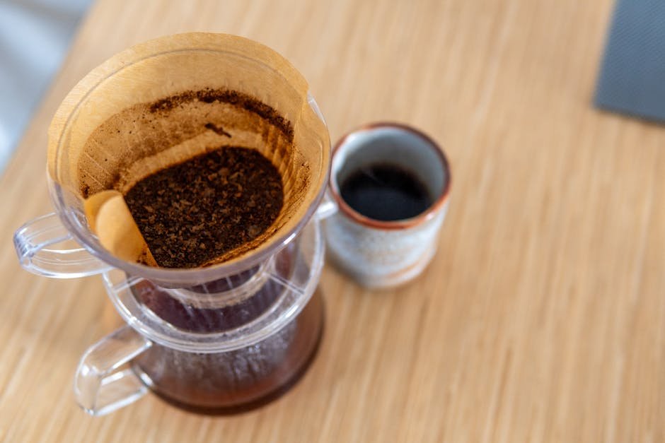 Top-down view of pour-over coffee in a filter next to a ceramic mug on a wooden table.