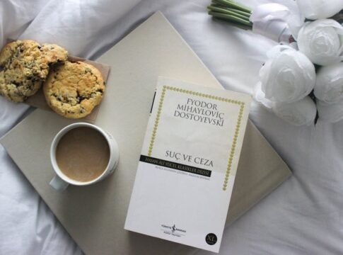Top view of a book, coffee, and cookies on a bed with white roses.