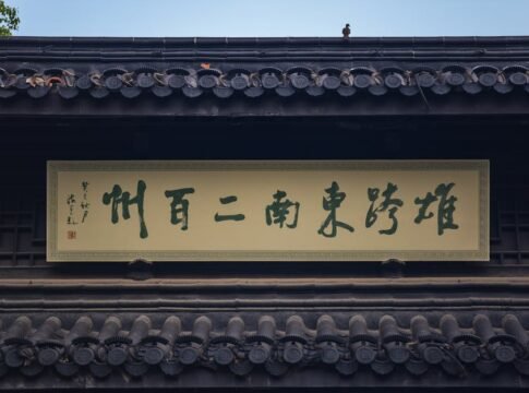 Traditional building exterior with Chinese characters on sign and decorative roof, featuring a small bird.