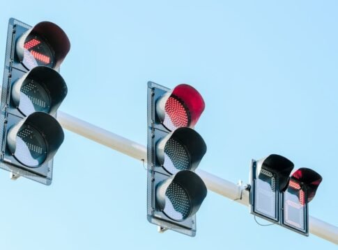 Traffic lights showing red against a clear blue sky on a sunny day.