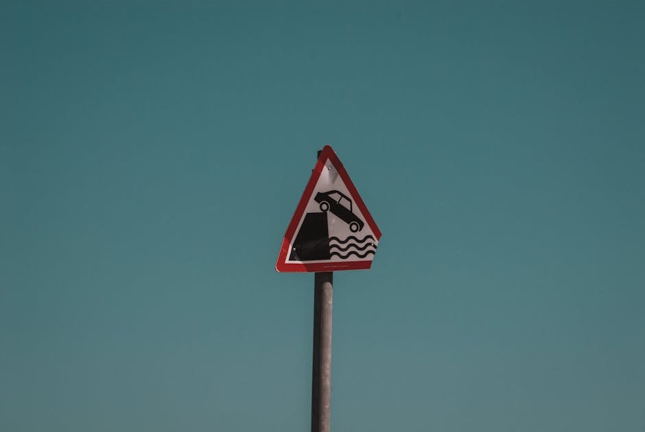 Ludhiana Municipal Corporation Faces Scrutiny Over Neglected Road Cavity Triangular traffic warning sign showing a car falling into water, set against a clear blue sky in Dublin, Ireland.