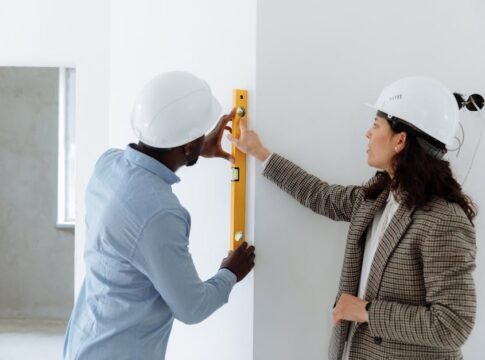 Two contractors using a level bar to check wall alignment inside a building.