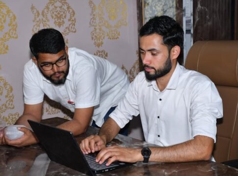 Two men working together at a desk, focused on a laptop, showcasing teamwork and collaboration.