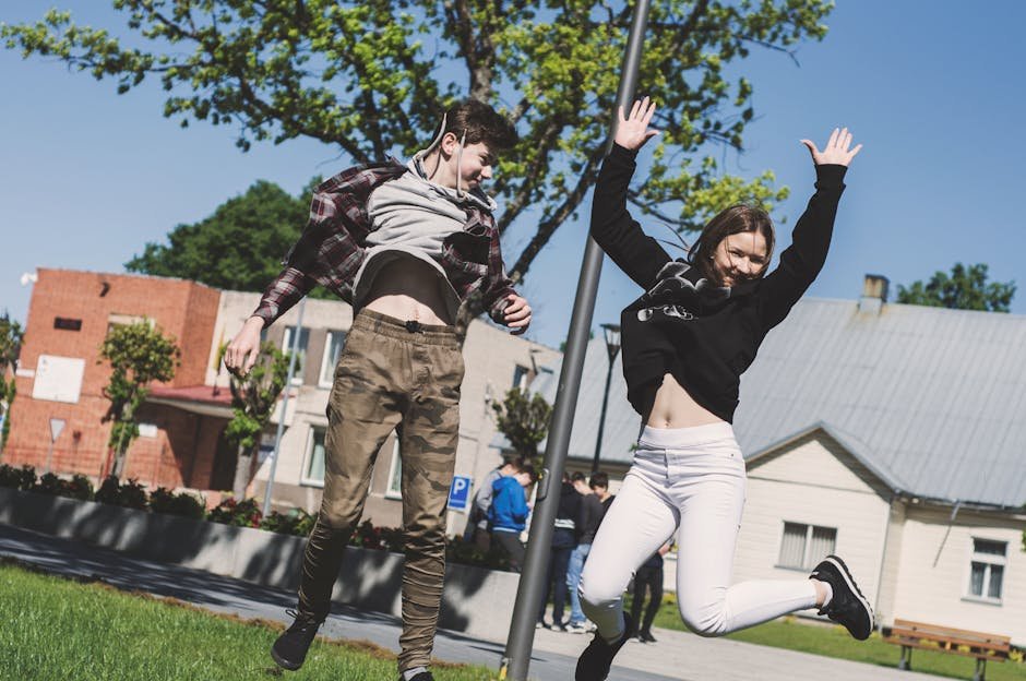 Two teenagers joyfully jumping outdoors in Šiluva, Lithuania under a bright blue sky. Captured in springtime.