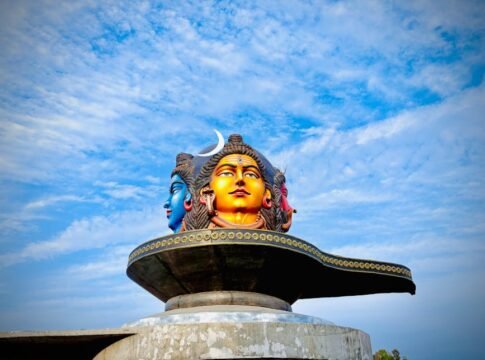 Vibrant three-headed Shiva statue under a blue sky in Pokhara, Nepal.