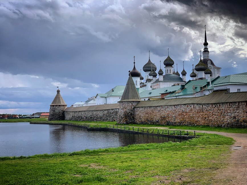 View of Solovetsky Monastery with its iconic domes reflecting on a calm river under a cloudy sky.