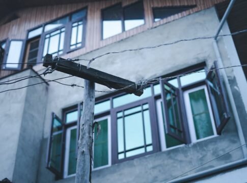Wooden power pole with electricity wires against an urban building with open windows in Srinagar.