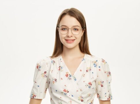 Young woman wearing glasses smiling in a floral outfit against a plain background.