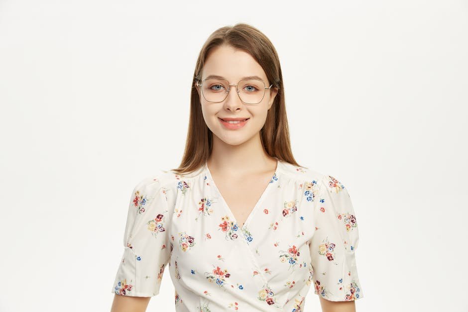 Young woman wearing glasses smiling in a floral outfit against a plain background.
