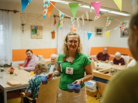 A caregiver serving drinks to elderly residents in a cheerful nursing home setting.