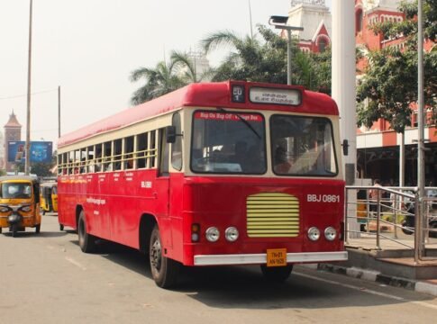 A classic red tour bus in Chennai offering hop-on hop-off services, with vibrant urban scenery.