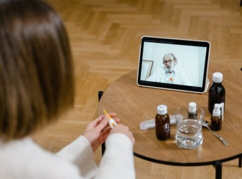 A doctor provides an online consultation via video call on a tablet, seen on a wooden table. A doctor provides an online consultation via video call on a tablet, seen on a wooden table.