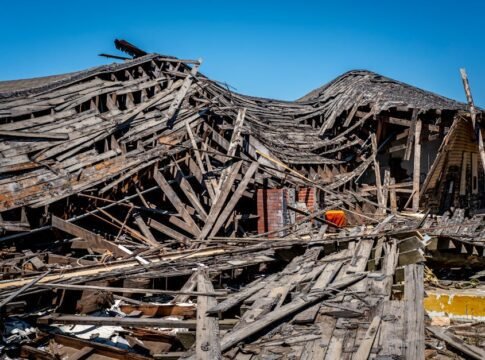 A dramatic view of a destroyed wooden building after a catastrophe, showing debris and structural failure.