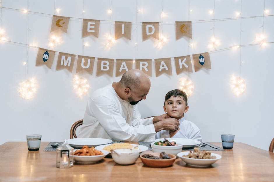 Kashmir Markets Receive Camels from Rajasthan Ahead of Eid-ul-Adha A father adjusts his son's shirt as they sit together celebrating Eid indoors with festive lights and food.