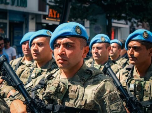 A group of soldiers in blue berets marching during a daytime military parade in the city.