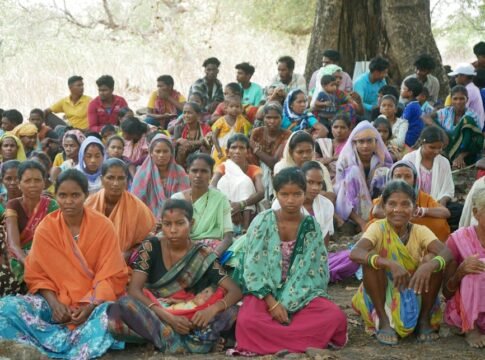A large group of people sitting outdoors under a tree, showcasing diversity and unity.