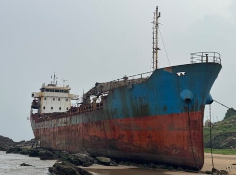 A large, rusted ship stranded on a rocky beach in Visakhapatnam, India.