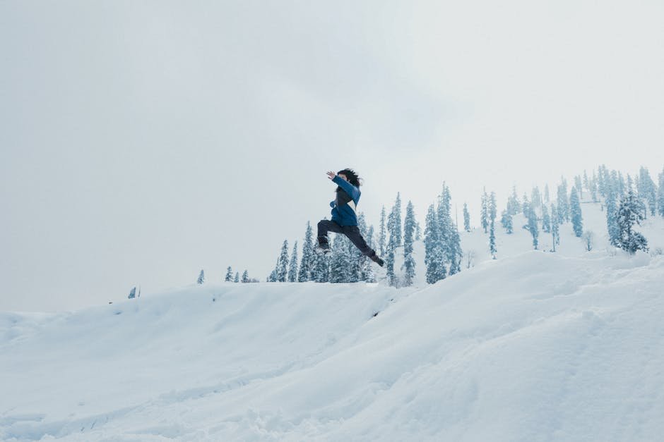 Kashmir Witnesses Unseasonal Snowfall in Upper Reaches, Heavy Rains Disrupt Plains A man leaps across a snow-covered hillside against a backdrop of trees in Gulmarg.