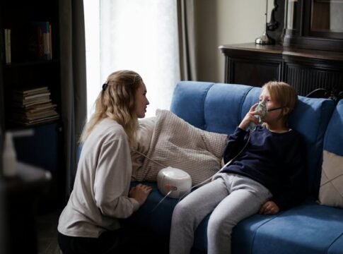 A mother assists her sick child using a nebulizer at home, providing comfort and care.