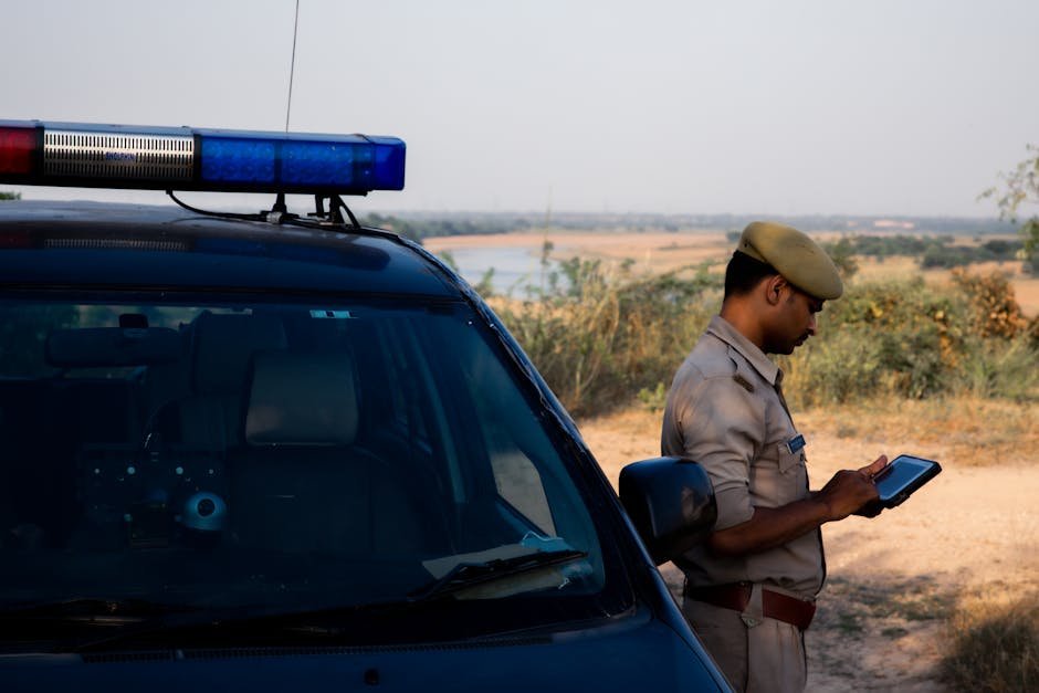 Punjab Police Deploy Over 1,200 Personnel for Jalandhar Rural Civic Polls A police officer using a tablet beside a patrol car in a rural outdoor setting.