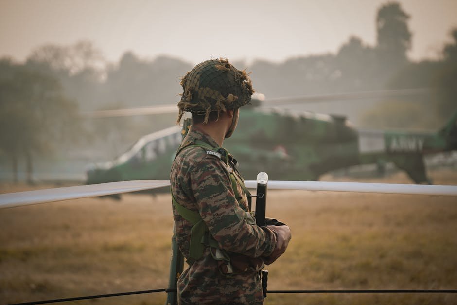 An Indian soldier stands guard in a field with a military helicopter in the background.
