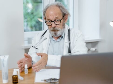 An elderly doctor in a white coat conducting an online medical consultation, focusing attentively.