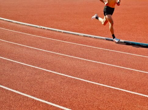 Athlete running on a red track in an outdoor stadium on a sunny day.
