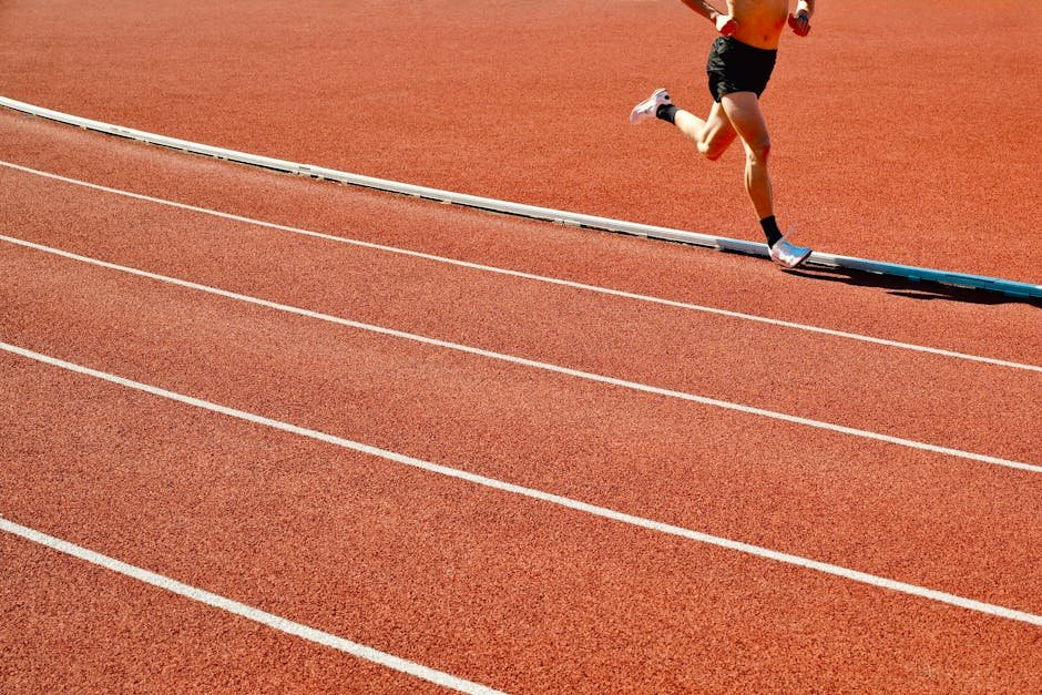 Punjab Sprinter Gurindervir Singh Inspires Young Athletes in Jalandhar Ahead of Record-Breaking Feat Athlete running on a red track in an outdoor stadium on a sunny day.