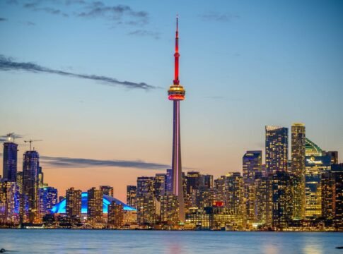 Beautiful sunset view of Toronto skyline with CN Tower and city lights reflecting on the lake.