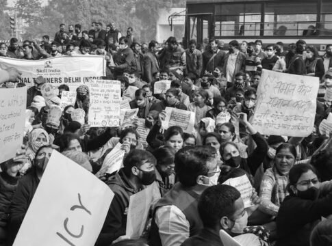 Black and white image of a crowded protest rally in Delhi advocating for policy reform.
