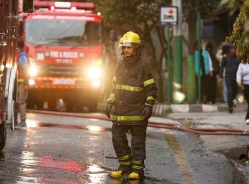 Firefighter in uniform stands near a fire truck in the street during an emergency operation.