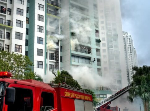 Firefighters respond to a building fire with smoke and emergency vehicles in an urban area.