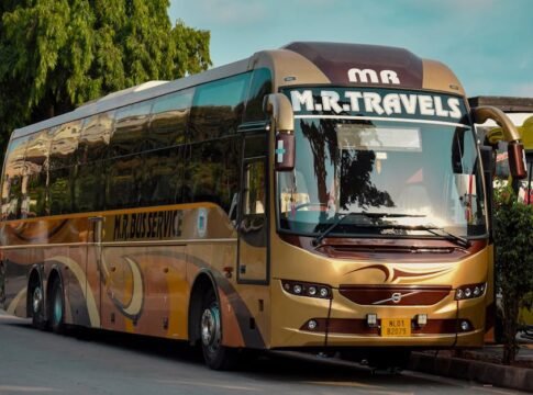 Golden luxury tour bus from M.R. Travels parked on street during the day with bright surroundings.