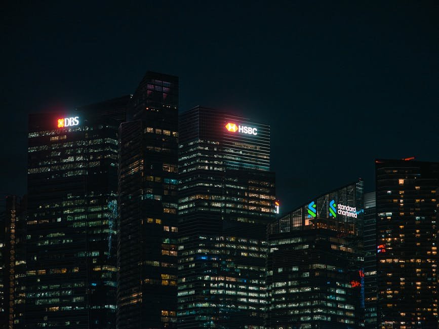 Private Banks’ Return on Equity Moderates in FY26 Amid NIM Pressure, Treasury Losses Illuminated city skyscrapers of major banks in Singapore's financial district at night.
