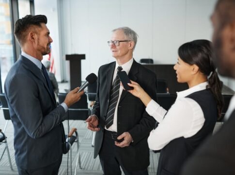 Journalists conduct an interview with a senior executive in a formal office setting.
