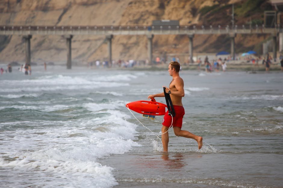 Punjab Initiative Empowers Youth as Emergency First Responders Lifeguard running into the ocean holding a rescue tube at a beach with a pier in the background.