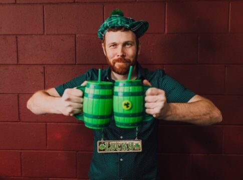 Man celebrating St. Patrick's Day indoors with green mugs and a lucky charm.