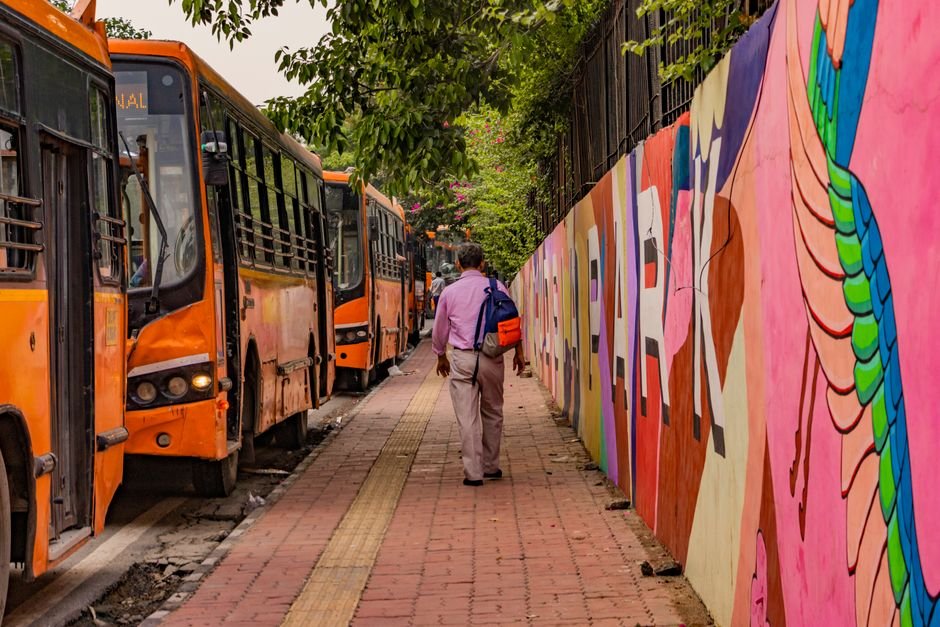 Delhi Government Announces Free DTC Bus Travel for NEET Re-test Candidates Man walking beside colorful street mural and lined buses in New Delhi, India.