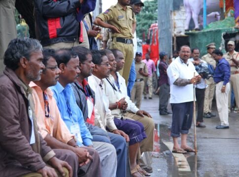 Men seated with police presence in a busy street, showcasing a public gathering or event.
