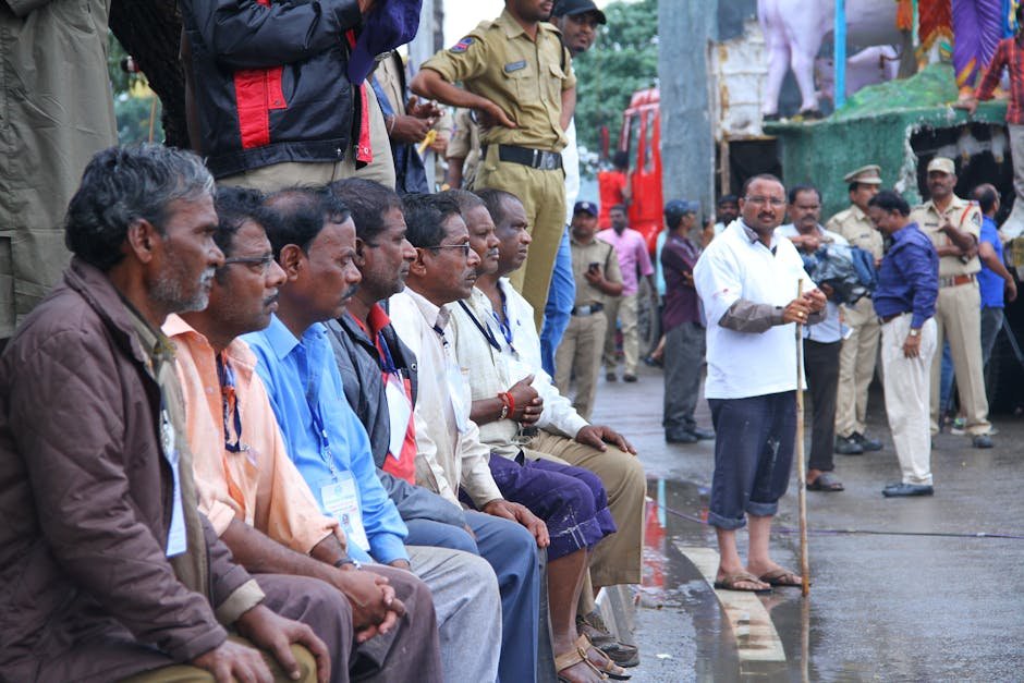 Ramanagara Mango Growers to Host Fair in Mangaluru Men seated with police presence in a busy street, showcasing a public gathering or event.